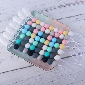Dettaglio di catenelle per ciuccio in perle di silicone colorate su un piatto e fondo in legno