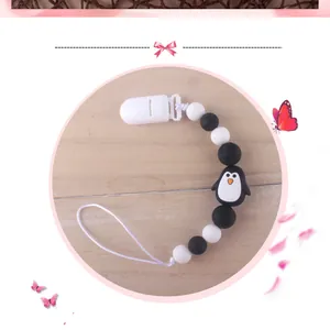 Detail of penguin silicone pacifier clip with black and white beads on wood background