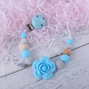 Baby silicone pacifier clip with blue rose bead and wooden accents on white wood