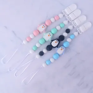 Detail of four colorful silicone pacifier clips with penguin beads on marble background