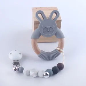 Close-up of baby teether set with grey silicone rabbit, wooden ring, and beaded clip