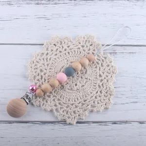 Détail de l'attache-tétine en hêtre et silicone avec clochette rose sur tapis de dentelle