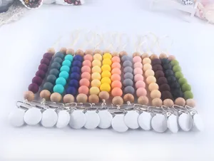 Flat lay of 14 colorful silicone and wood baby pacifier clips on a white background