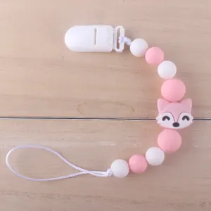 Macro detail of a pink silicone baby pacifier clip with a cartoon fox bead on wood