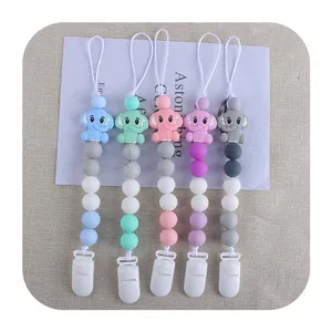 Five colorful silicone elephant pacifier clips with plastic clamps on a beige fabric background