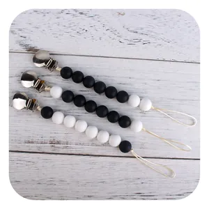 Three sets of silicone beaded pacifier clips with silver metal buckles on white wood base