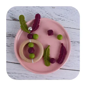 Baby teething ring with wood handle, colorful silicone beads, feathers, and bell in a plate