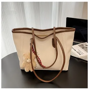 Detail of cream white tote bag with brown trim, cute bear charm and ribbon decor