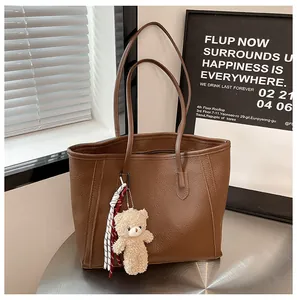 Detail of dark brown pebble leather tote bag with plush bear charm and long straps
