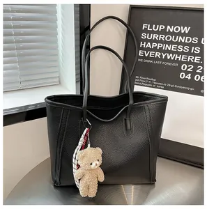 Detail of black pebbled leather tote bag with a cute plush bear charm on metal table