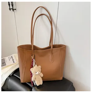 Detail of classic brown litchi leather tote bag with a cute plush bear pendant accessory