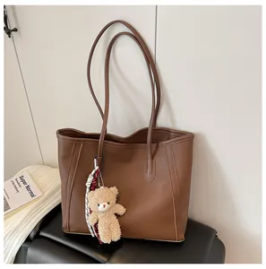 Close-up of brown faux leather tote bag with cute plush bear charm and long straps