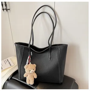 Detail of black pebbled leather tote bag with a cute brown plush bear charm attached