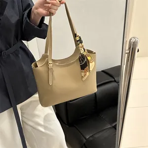Chic khaki leather tote bag with printed silk scarf detail held by model in elegant setting