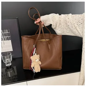 Close-up of brown litchi pattern leather tote bag with cute plush bear charm decoration