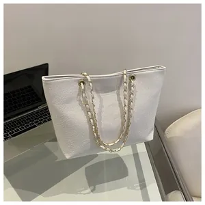 Detail of white crocodile pattern tote bag with gold chain strap on office desk