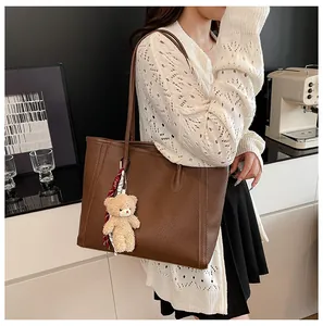 Detail of dark brown faux leather tote with plush bear charm and plaid scarf accent