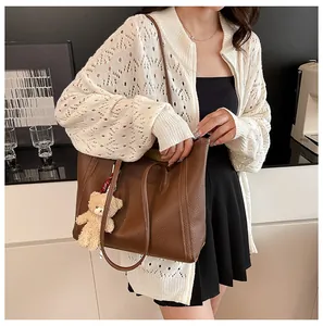 Brown faux leather tote bag with plush bear charm shown in a lifestyle street style look