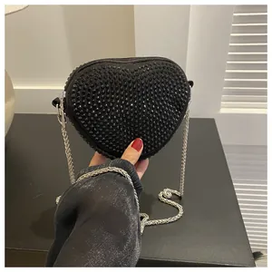 Detail of heart-shaped black crossbody bag with stud accents and silver chain strap