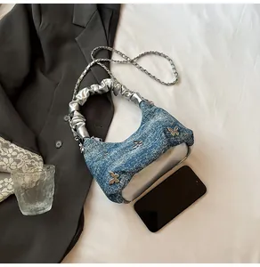 Détail d'un sac bandoulière en jean bleu avec rivets papillon argentés et anse plissée