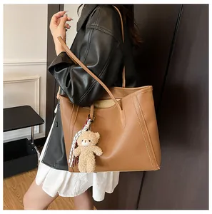 Close-up of brown pebbled leather tote bag with a cute plush bear and scarf charm