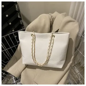 White crocodile embossed tote bag with gold chain strap on stylish beige coat background