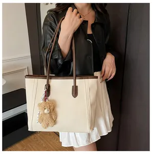 Detail of off-white leather tote bag with brown contrast trim and plush bear charm