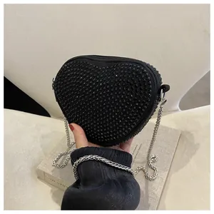 Close-up of heart-shaped black rhinestone bag with silver chain strap and velvet texture