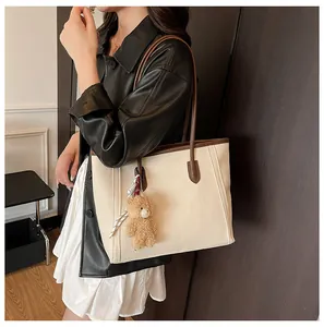 Detail of cream tote bag with litchi texture, brown straps, and a cute teddy bear charm