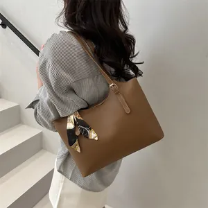 Detail of a brown leather tote bag featuring a stylish decorative silk scarf on handle
