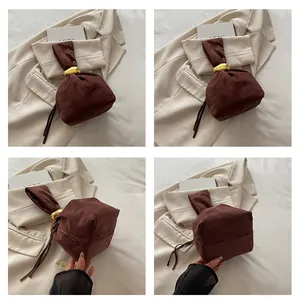 Close-up of brown suede handbag featuring knotted handle and gold metal fastener