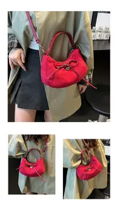 Détail d'un sac demi-lune en daim rouge avec nœud décoratif et pendentif en cœur