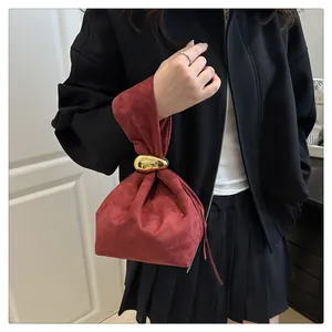 Close-up of burgundy suede bucket bag featuring elegant gold wavy metal handle attachment