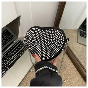 Macro shot of black heart-shaped bag with silver rhinestones and metal chain strap