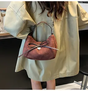 Détail du cabas en daim marron foncé avec un nœud en cuir et une breloque cœur doré