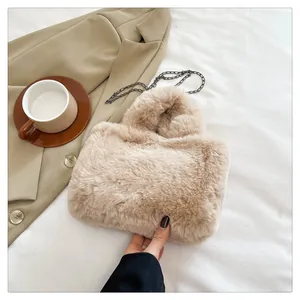 Detail view of a beige faux fur crossbody bag with dark metal chain strap on a white fabric