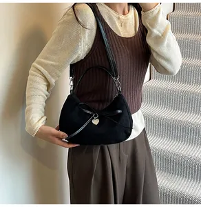 Détail du sac croissant en daim noir avec nœud décoratif et pendentif cœur argenté