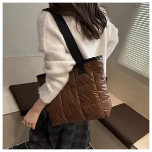 Detail of a large brown quilted tote bag with black wide straps on a fashion model