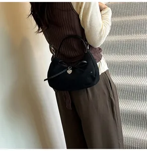 Détail du sac demi-lune noir en daim avec nœud décoratif et pendentif cœur argenté