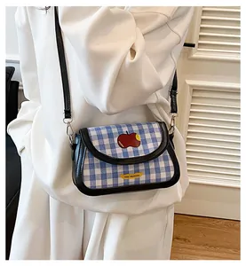 Close-up of blue checkered square bag featuring red apple patch and black strap