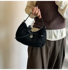 Détail du sac hobo en daim noir avec nœud en ruban et pendentif cœur argenté