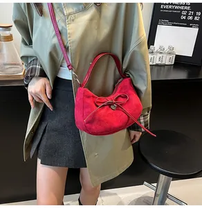 Détail du sac bandoulière en daim rouge avec pendentif coeur porté par un mannequin
