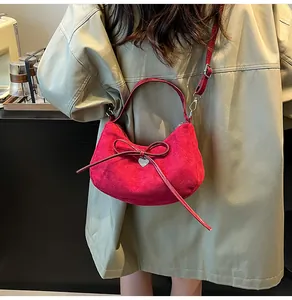 Détail du sac croissant en daim rouge avec nœud en cuir et pendentif cœur sur modèle