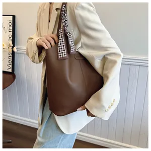 Detail of a large brown pebble leather tote bag with a checkered silk scarf on the handle