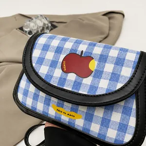 Close-up of blue plaid canvas shoulder bag with red apple patch and black leather trim