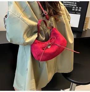 Détail du sac cabas en daim rouge avec nœud et breloque cœur porté par un mannequin