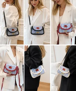 Detail view of blue gingham crossbody bag with red apple patch on model.