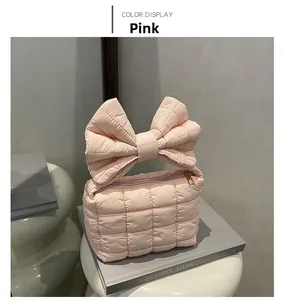 Detailed view of pink quilted handbag with large bow handle and gold zipper on books
