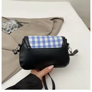 Detail of hand holding plaid flap crossbody bag with black leather and metal hardware