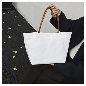 Detalle del bolso tote de lona blanca con asas de cuero marrón y costura de calidad